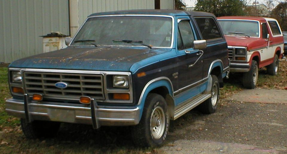 Faded blue Ford Bronco SUV front 3/4 view with a red-and-white Bronco behind it