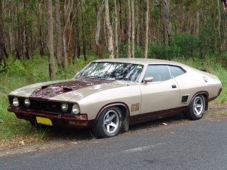 1991 Ford Bronco - This 1970s Ford Falcon coupe is seen from a 3/4 front angle, parked on the side of a road with trees in the background.