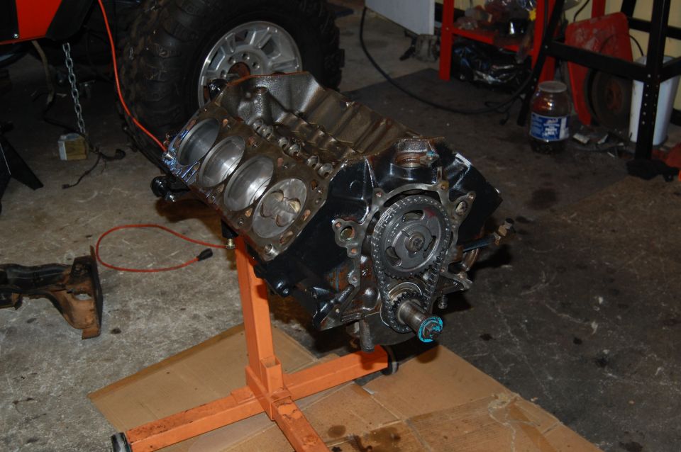 Engine block on orange stand, with a large tire and part of a vehicle in the background