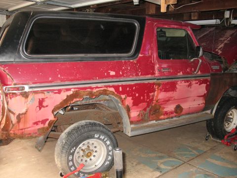 1978 Ford Bronco - This heavily rusted red Ford Bronco is in a garage, showing significant body damage.