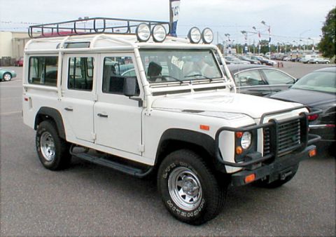 1983 Ford Bronco - This white Land Rover Defender 110 is parked in a lot with other vehicles.
