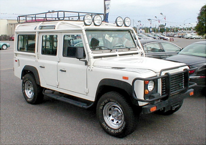 White Land Rover Defender 110 with roof rack and driving lights, front-right view