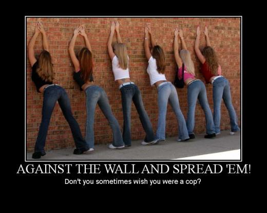 six women in jeans leaning against a brick wall, hands up