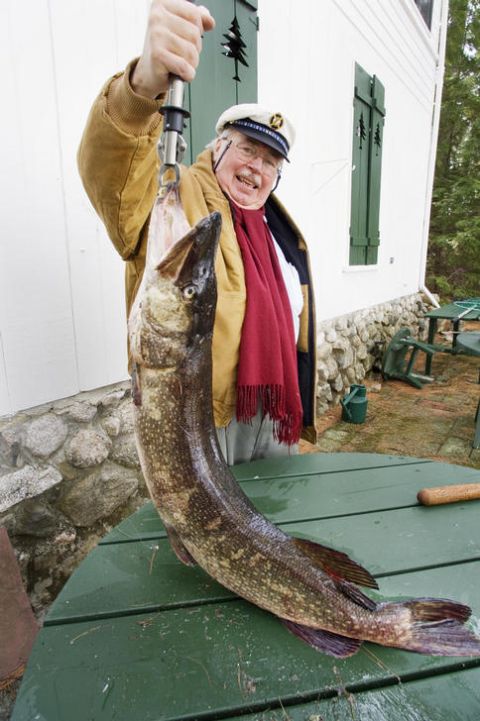 1990 Ford Bronco - A man proudly displays a large fish he has caught, with a building and outdoor furniture visible behind him.