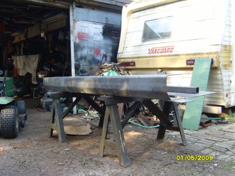 1989 Ford Bronco - A fabricated metal bumper is supported by sawhorses in a cluttered outdoor workshop area.