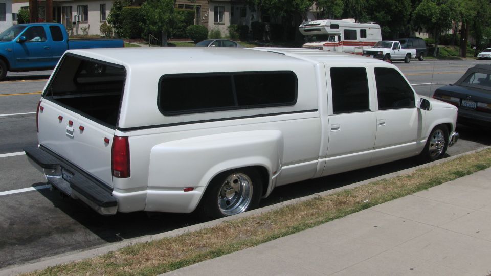 white extended cab dually pickup truck with a camper shell parked on street