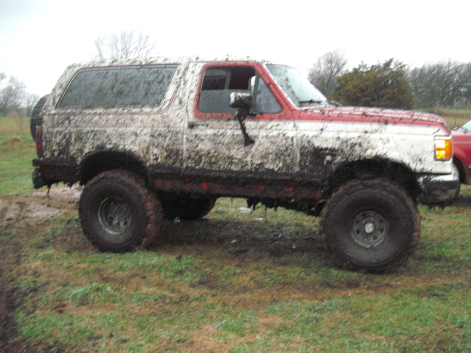 Mud-covered 1991 Ford Bronco, 3/4 front view, white and red
