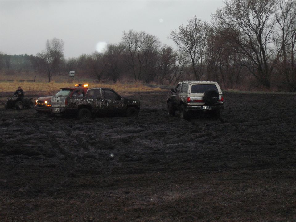 1991 Ford Bronco and a muddy pickup truck stuck in mud, with an ATV nearby