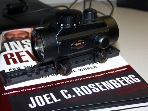 1986 Ford Bronco - A tactical gun sight is placed on top of books, one of which features a portrait and text.