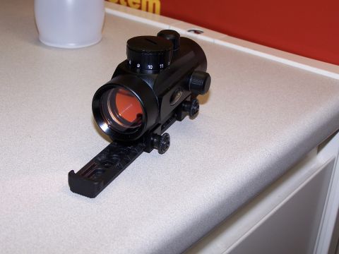 1986 Ford Bronco - A black red dot sight with an orange lens and a dial marked 9, 10, 11 is shown on a textured surface.