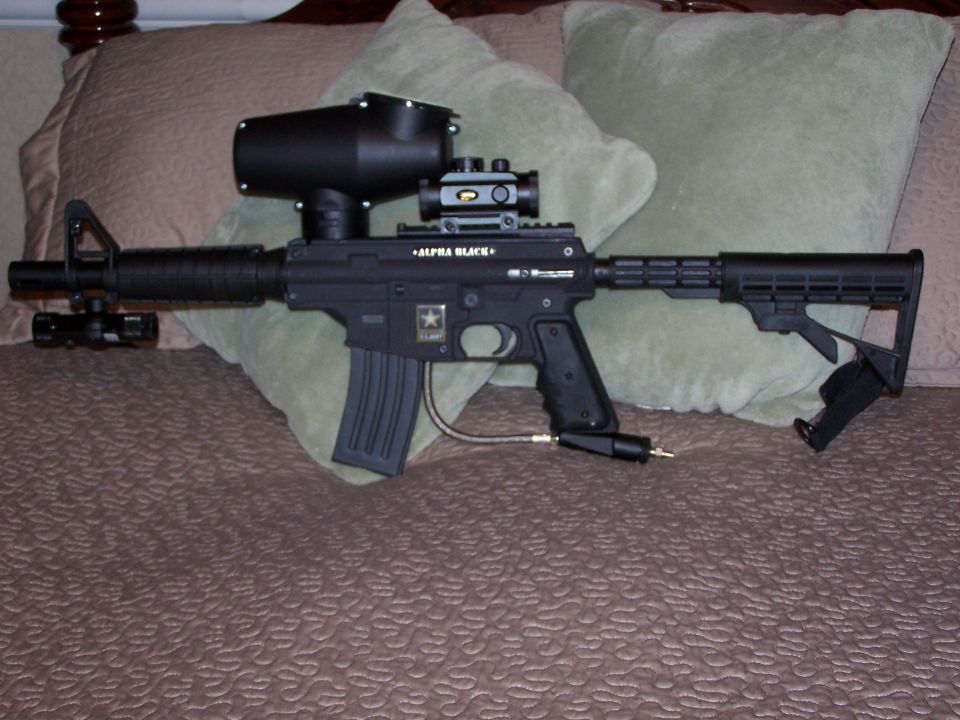 Black paintball gun with hopper and scope, labeled "ALPHA BLACK" and "ARMY"