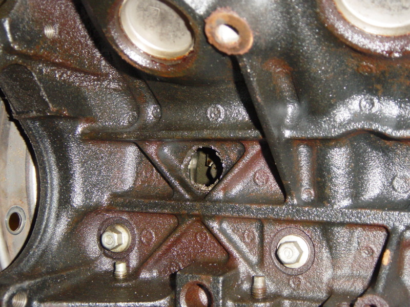 Close-up of a cast iron engine block showing a hole with damaged edges