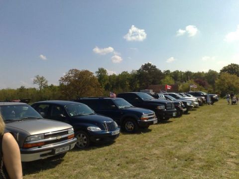 1991 Ford LTD Crown Victoria - A row of vehicles, including SUVs and cars, are parked on a grassy field on a sunny day.