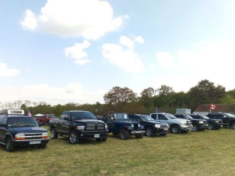 1991 Ford LTD Crown Victoria - A line of trucks and SUVs are parked on a grassy field with trees in the background.