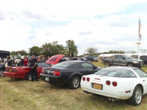 1991 Ford LTD Crown Victoria - Several cars are parked on a grassy field with people milling about, under a cloudy sky.
