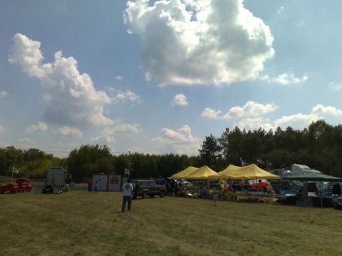 1991 Ford LTD Crown Victoria - An outdoor gathering features various vehicles and vendor tents under a bright, cloudy sky.
