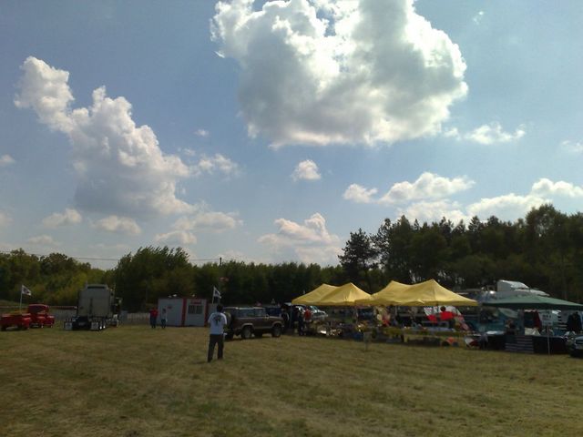 Outdoor event with tents, trucks, and cars on a grassy field under a cloudy sky