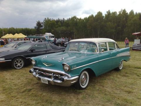 1991 Ford LTD Crown Victoria - A teal and white 1957 Chevrolet Bel Air sedan is parked on a grassy field with other vehicles and tents in the background.