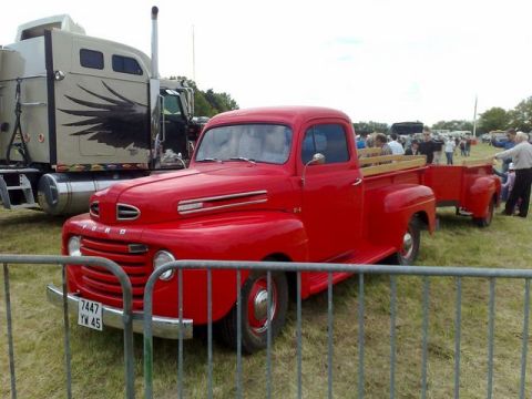 1991 Ford LTD Crown Victoria - A classic red Ford F-series pickup truck from the late 1940s is displayed at an event, with a large semi-truck in the background.