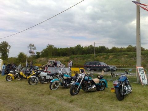 1991 Ford LTD Crown Victoria - A collection of motorcycles are parked on the grass, with people and vehicles in the background.