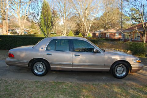 1996 Mercury Grand Marquis - Tan sedan with wire wheels parked on a residential street.