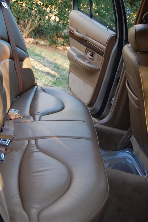 1996 Mercury Grand Marquis - The interior of a car shows tan leather seats and a door panel with wood trim, with the rear passenger door open.