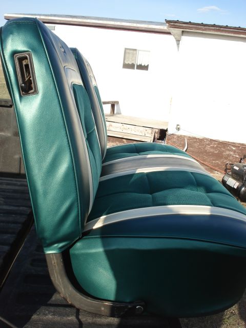1979 Ford F-150 - A green and gray car seat is shown from the side, with a white building in the background.