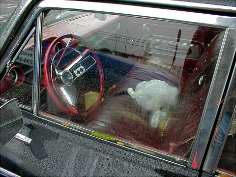1983 Ford Bronco - Interior view of a car with a red steering wheel and seats, seen through a wet window.