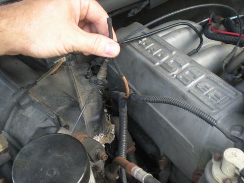 1990 Ford Bronco - Close-up of a hand adjusting a vacuum line in the engine bay of a 1990 Ford Bronco.