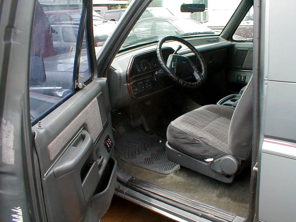 Gray interior of Ford truck through open driver door, showing seat, dash and steering wheel