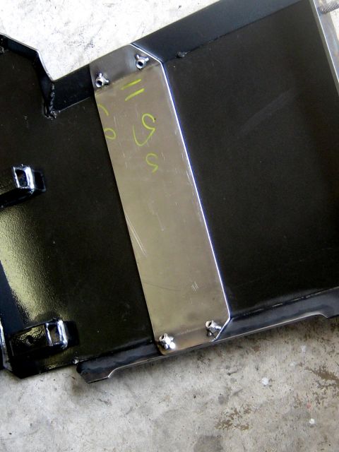 1996 Ford Bronco - A close-up view of a black metal part with a silver metal plate attached with rivets. Yellow markings are visible on the silver plate.