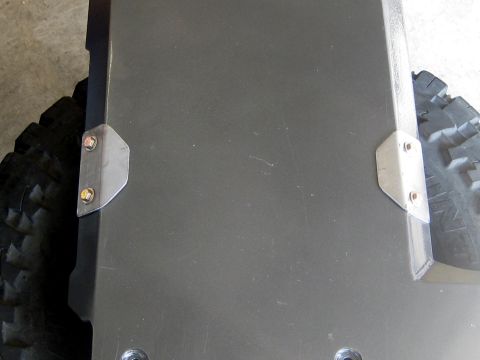 1996 Ford Bronco - A close-up view of a dark gray metal panel, possibly a skid plate, mounted with two metal brackets and bolts, positioned over a portion of…