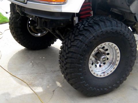 1996 Ford Bronco - A close-up view of the front passenger side wheel and suspension of a lifted Ford Bronco. The vehicle features large, aggressive off-road t…