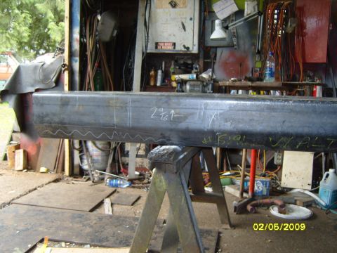 1989 Ford Bronco - A large metal beam, likely a vehicle part, is marked with white and yellow chalk measurements and labels. The beam is supported by a metal…