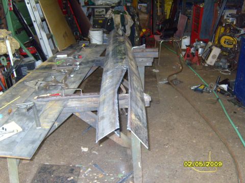 1989 Ford Bronco - A metal fabrication project is underway in a workshop. A long, bent metal piece is the central focus, with various tools and materials scat…
