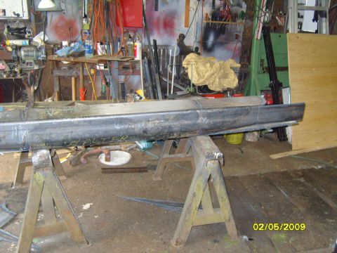 1989 Ford Bronco - A long, dark metal beam is supported by two sawhorses in a workshop. The beam has white markings on it, including the word "HALTER".