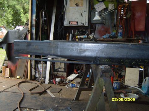 1989 Ford Bronco - A metal beam is supported by sawhorses in a cluttered workshop. The beam has markings on it and appears to be part of a project. The backgr…