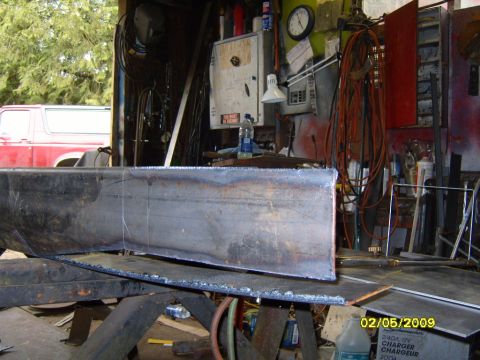 1989 Ford Bronco - A large, cut piece of metal tubing is positioned in the foreground of a workshop, with a red 1989 Ford Bronco visible in the background. Th…
