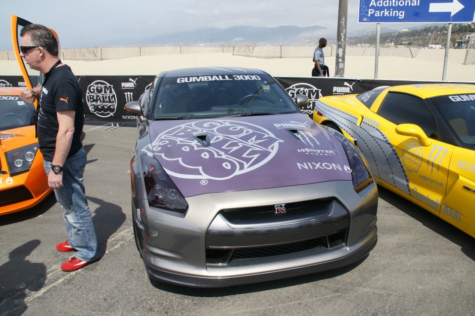 Grey Nissan GT-R with Gumball 3000 graphic, yellow Corvette, and orange Lamborghini.