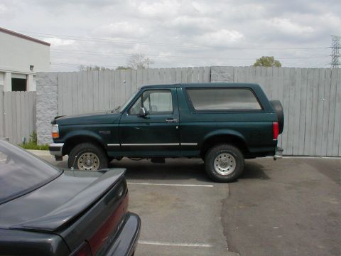 1983 Ford Bronco - This green Ford Bronco, likely from the early 1990s, is parked in a lot with a spare tire mounted on the rear.