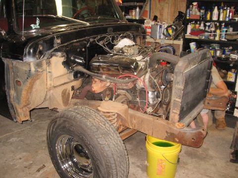 1966 Ford F-100 - The front end of a black pickup truck is shown, with the hood removed to reveal the engine and radiator. A yellow bucket filled with green…