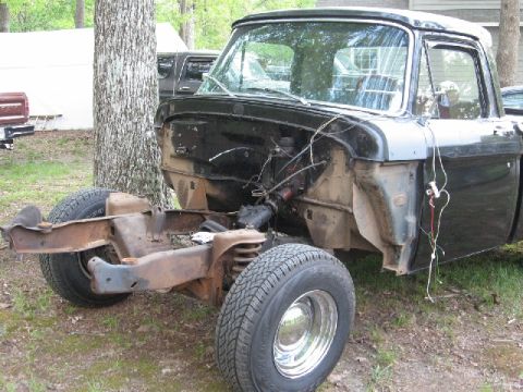 1966 Ford F-100 - A black Ford F-100 pickup truck chassis is shown with the body removed from the front. The front tires and suspension components are visibl…