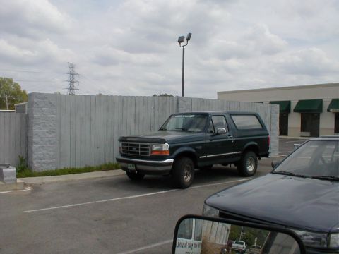 1983 Ford Bronco - A dark green Ford Bronco is parked in a lot, with another vehicle partially visible in the foreground.