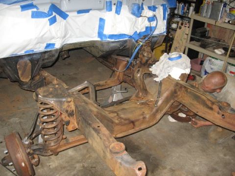 1966 Ford F-100 - A person works on the heavily rusted frame of a vehicle, with the body covered for protection.