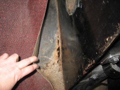 1966 Ford F-100 - A hand points to significant rust damage on a vehicle's metal panel, adjacent to the interior carpet.