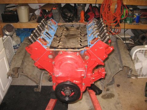 1966 Ford F-100 - A red V8 engine block is disassembled and mounted on an engine stand in a garage setting.