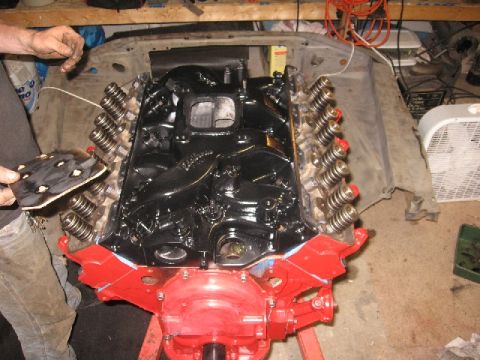 1966 Ford F-100 - Top-down view of a V8 engine mid-build on a stand, with freshly painted red timing cover and front accessory brackets, a black intake manif…