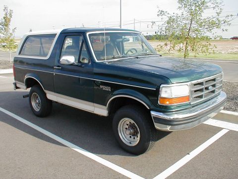 1983 Ford Bronco - This Ford Bronco is parked in a lot, showing its front three-quarter view with a dark green body and white roof.