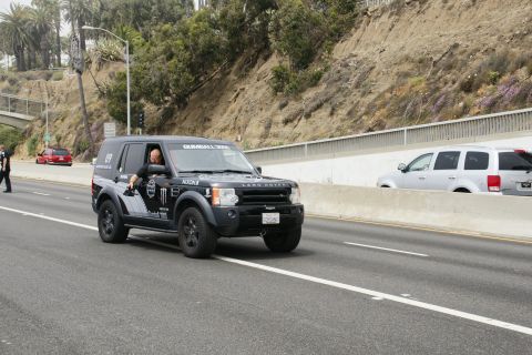 1993 Ford Taurus - A black Land Rover Discovery with Gumball 3000 branding is seen on the highway, with other vehicles in the background.