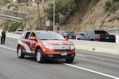 1993 Ford Taurus - An orange Ford Edge SUV with racing decals drives on a highway, with other vehicles visible in the background.